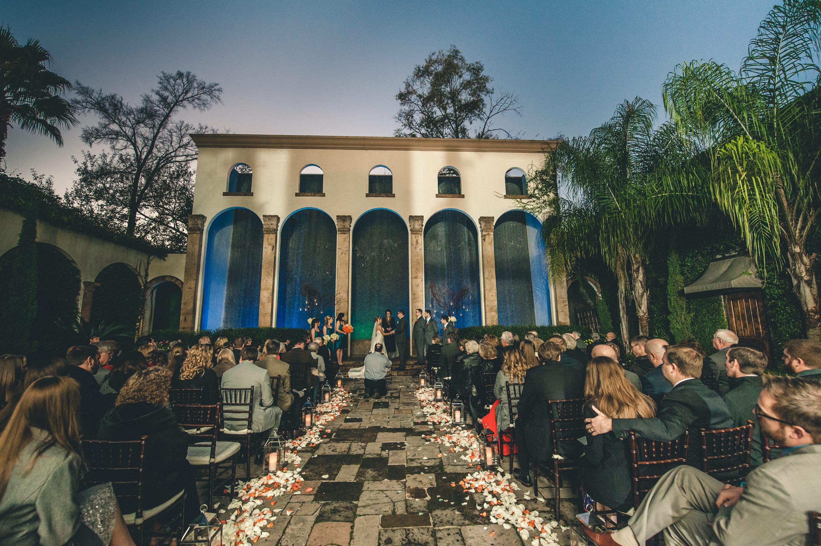 Twilight ceremony before the illuminated Waterwall arches at The Bell Tower on 34th, with a petal-lined stone aisle