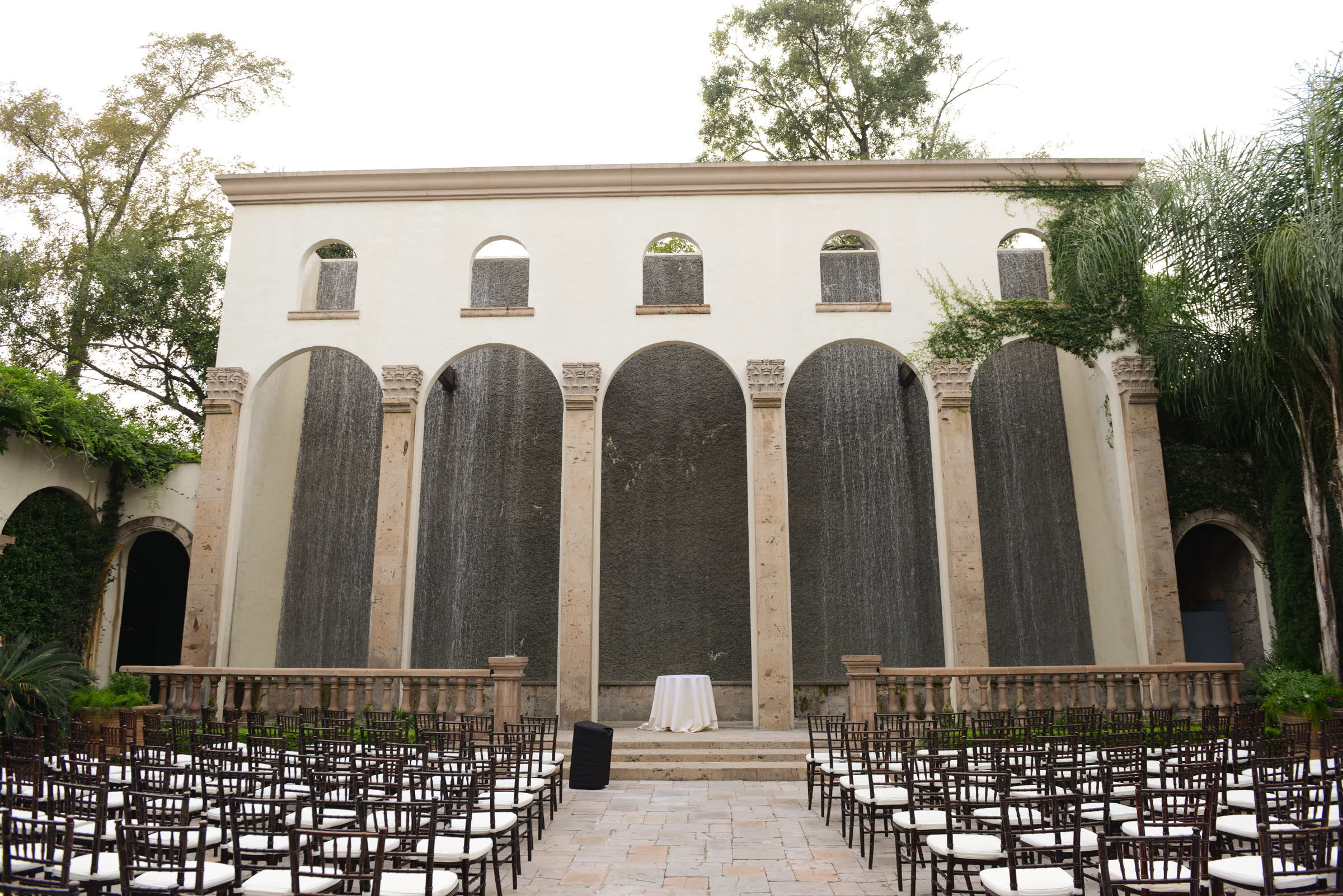 The signature cascading Waterwall and stone arches at The Bell Tower on 34th, an event courtyard set with chairs in daylight
