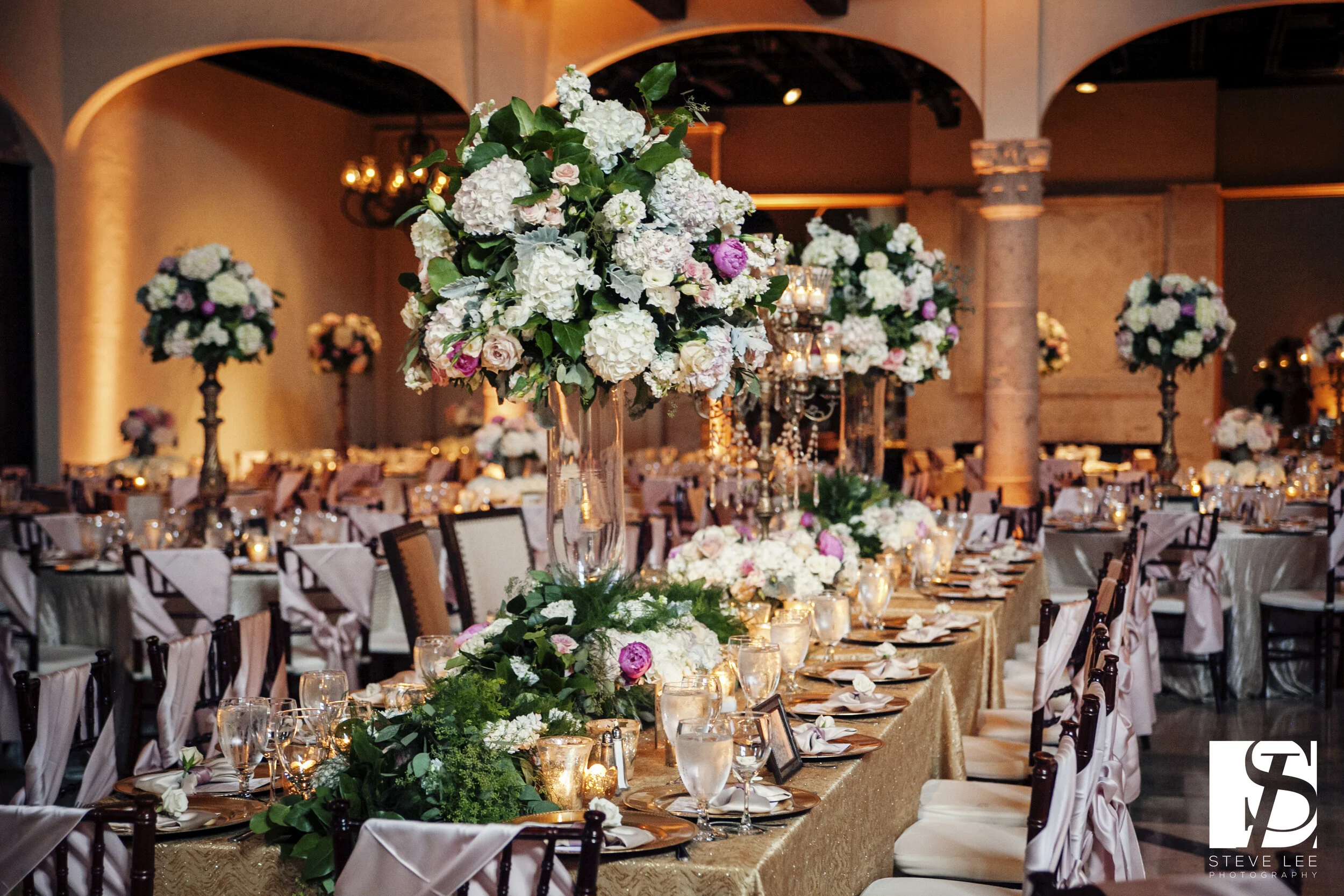 Grand ballroom reception with tall florals, gold linens and candlelight